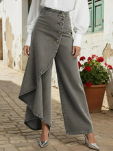 Woman wearing high-waisted gray denim wide-leg pants with asymmetric buttoned overlay and silver heels