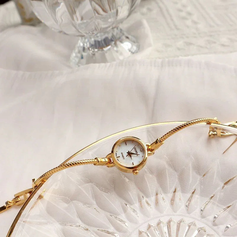 Gold minimalist bracelet watch with round white dial on sheer fabric background