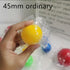 Hand holding a yellow 45mm plastic ball in clear wrapper, assorted colored balls in background