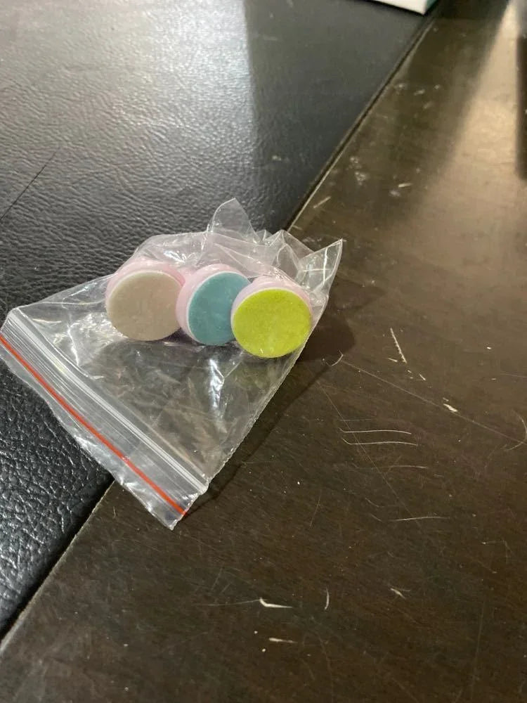 Four multicolored round tablets in a small plastic bag on a dark surface