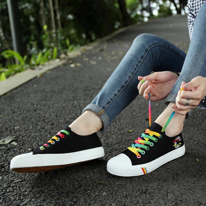 Black canvas sneakers with rainbow laces and white rubber toe, worn with skinny jeans outdoors