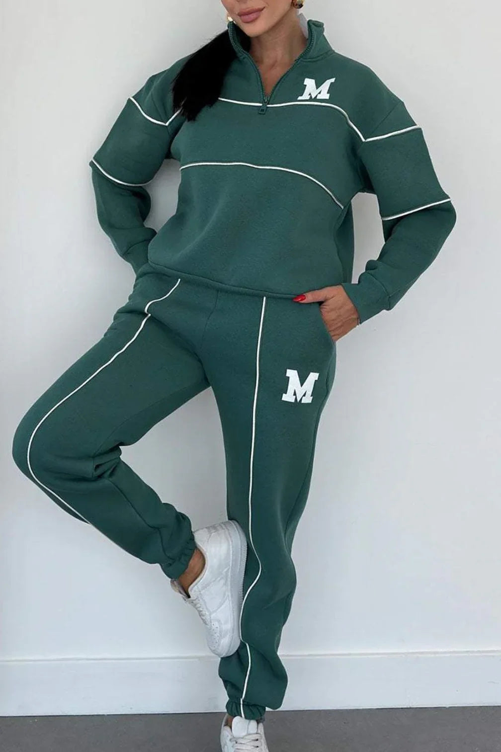 Woman wearing green oversized tracksuit set with white piping, quarter zip top, relaxed fit pants.