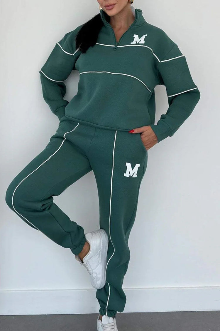 Woman wearing green oversized tracksuit set with white piping, quarter zip top, relaxed fit pants.