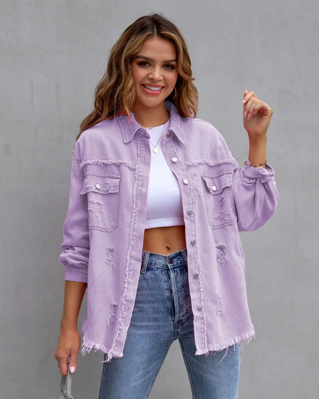 Woman wearing oversized light purple distressed denim jacket, white crop top, and blue jeans