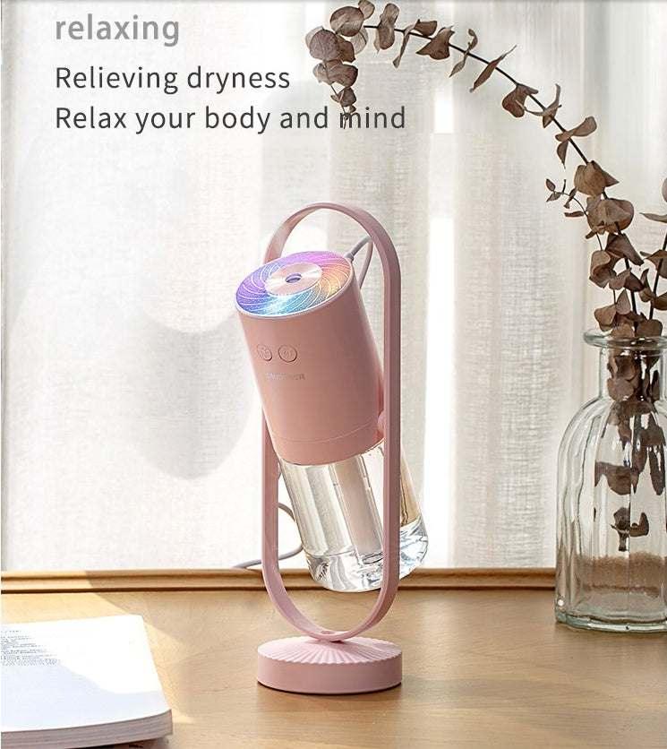 Pink portable humidifier with rainbow LED light, modern design, placed on a wooden table.