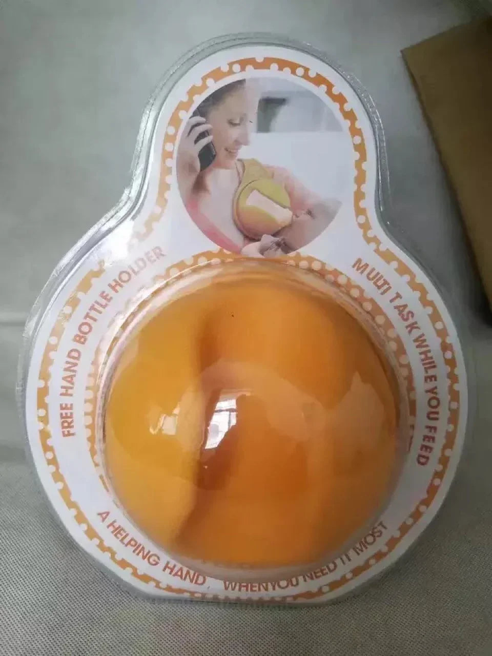 Free hand baby bottle holder in orange, packaged with multitasking mother feeding baby illustration.