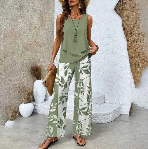 Woman wearing sleeveless sage green layered top and wide-leg white pants with green leaf print