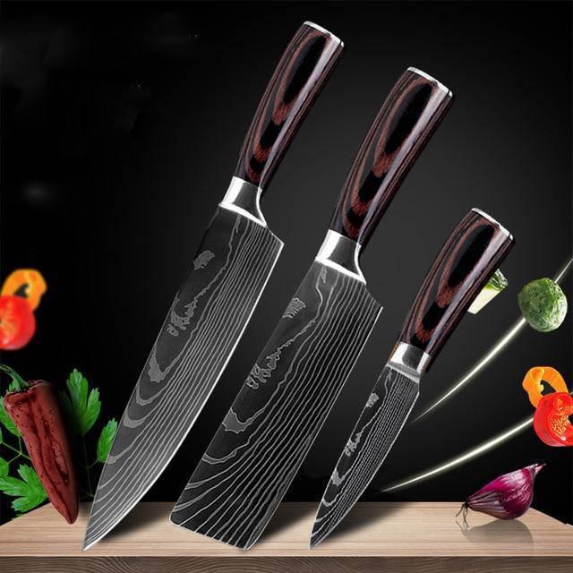 Set of three black Damascus steel kitchen knives with dark wood handles, displayed on a wooden surface.
