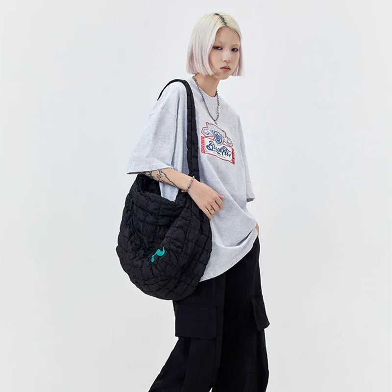 Woman in oversized grey graphic t-shirt, black cargo pants, and quilted black shoulder bag.