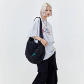 Woman in oversized grey graphic t-shirt, black cargo pants, and quilted black shoulder bag.
