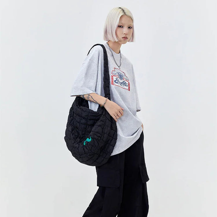 Woman in oversized grey graphic t-shirt, black cargo pants, and quilted black shoulder bag.