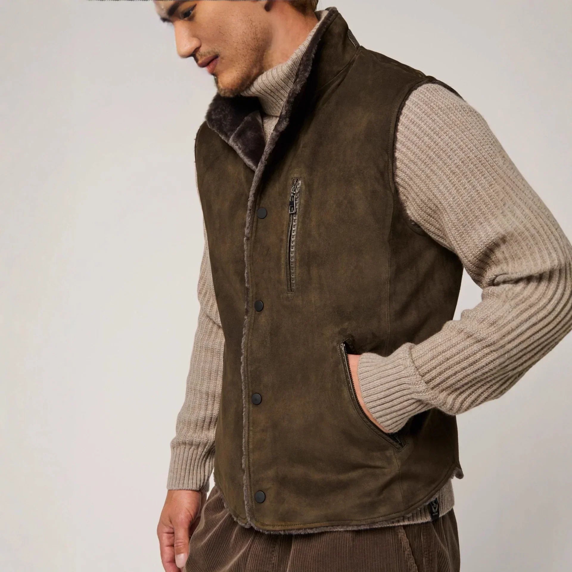 Man wearing brown suede shearling vest over ribbed beige sweater, casual streetwear style.