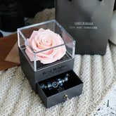 Black gift box with preserved pink rose, drawer containing blue beaded bracelet, on knit surface