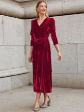 Woman wearing a red velvet wrap dress with long sleeves and a midi length, standing outdoors.