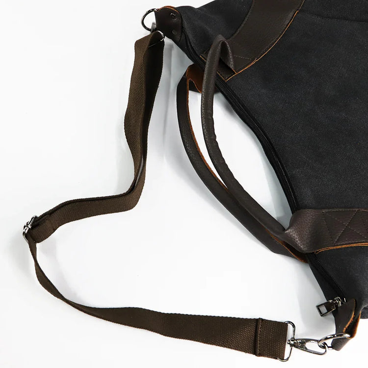Black canvas shoulder bag with brown leather trim and adjustable strap, modern streetwear style