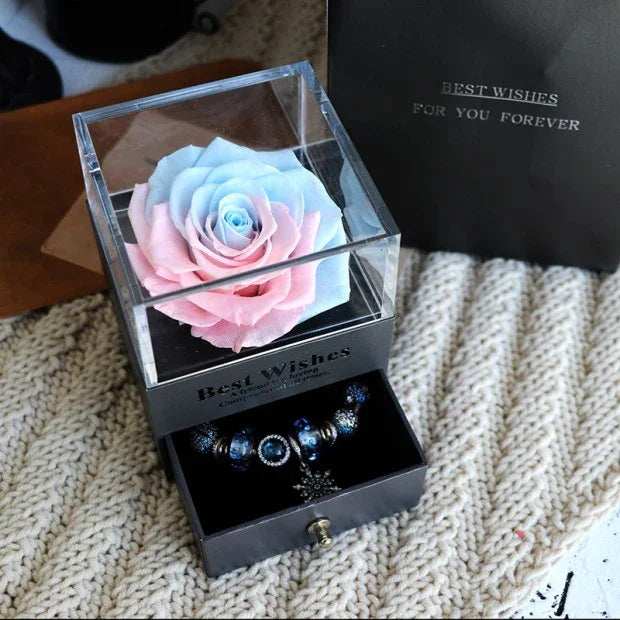 Blue and pink preserved rose in clear display box with dark beaded bracelet below