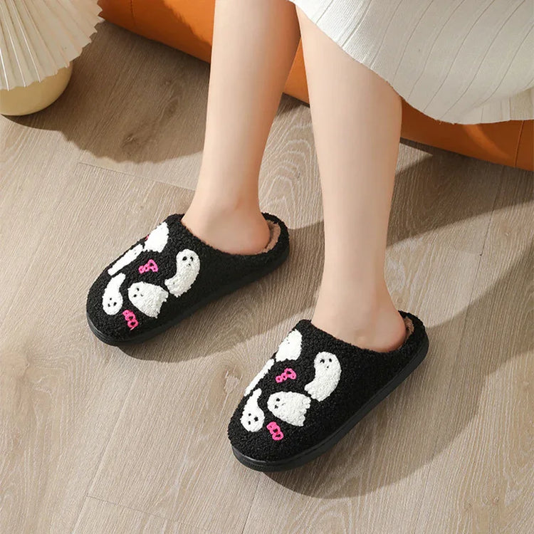 Black fuzzy slip-on slippers with white ghost patterns and pink bows, cozy indoor fit