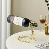 Gold chain wine bottle holder on white table with red wine glass, modern decor