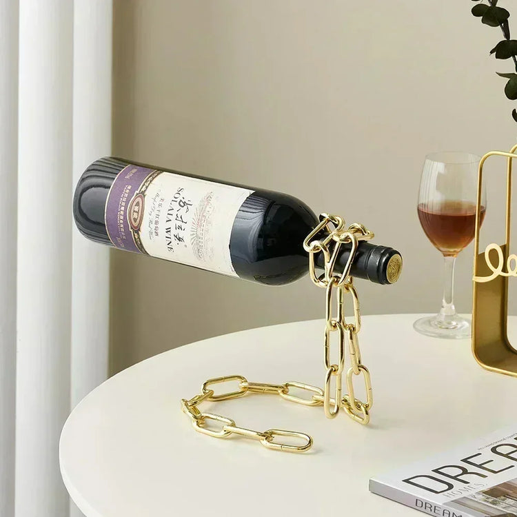 Gold chain wine bottle holder on white table with red wine glass, modern decor