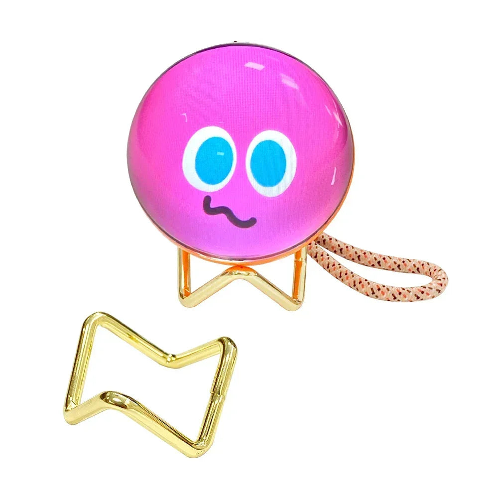Cute pink round accessory with emoji face, gold metal stand, and woven wrist strap