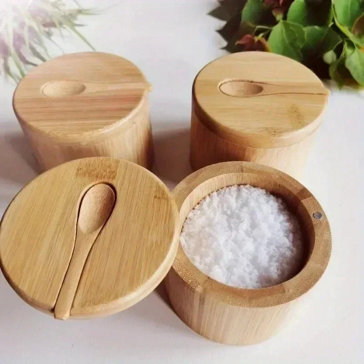 Round bamboo spice containers with lids and small spoons, one filled with salt, on a white surface