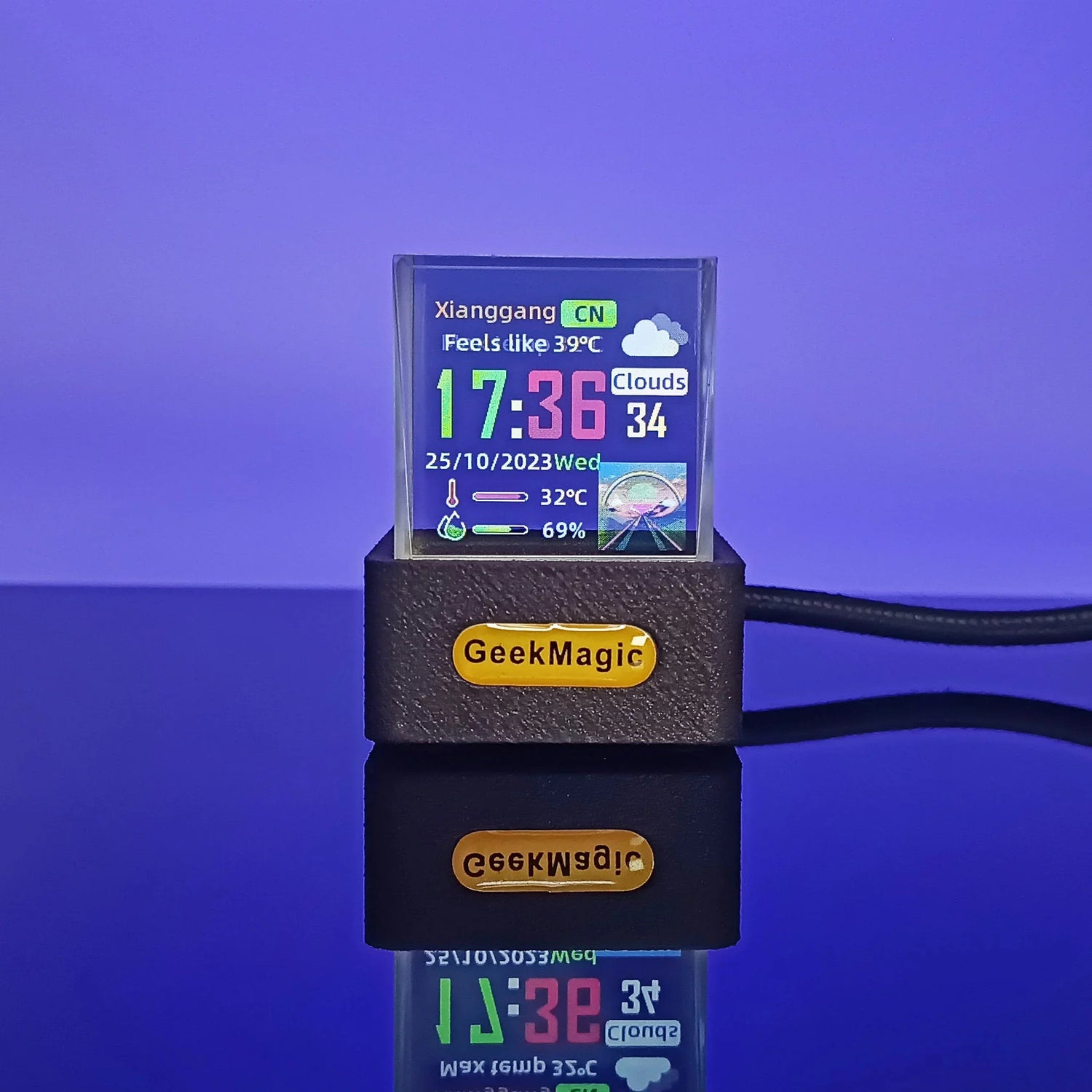 Small desktop digital weather clock with colorful display on black stand, purple background.