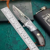 Patterned steel knife with engraved handle and dark wood grip, placed next to a ruler.