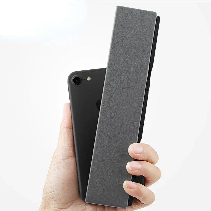 Hand holding a slim black smartphone and a gray folding tech accessory, minimalist style