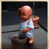 Ceramic monk figurine in blue robe with basket, pouring water into a bowl, minimalist decor