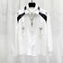 White long sleeve button-up shirt with black faux leather shoulder accents, metal buckle straps, and a relaxed fit.