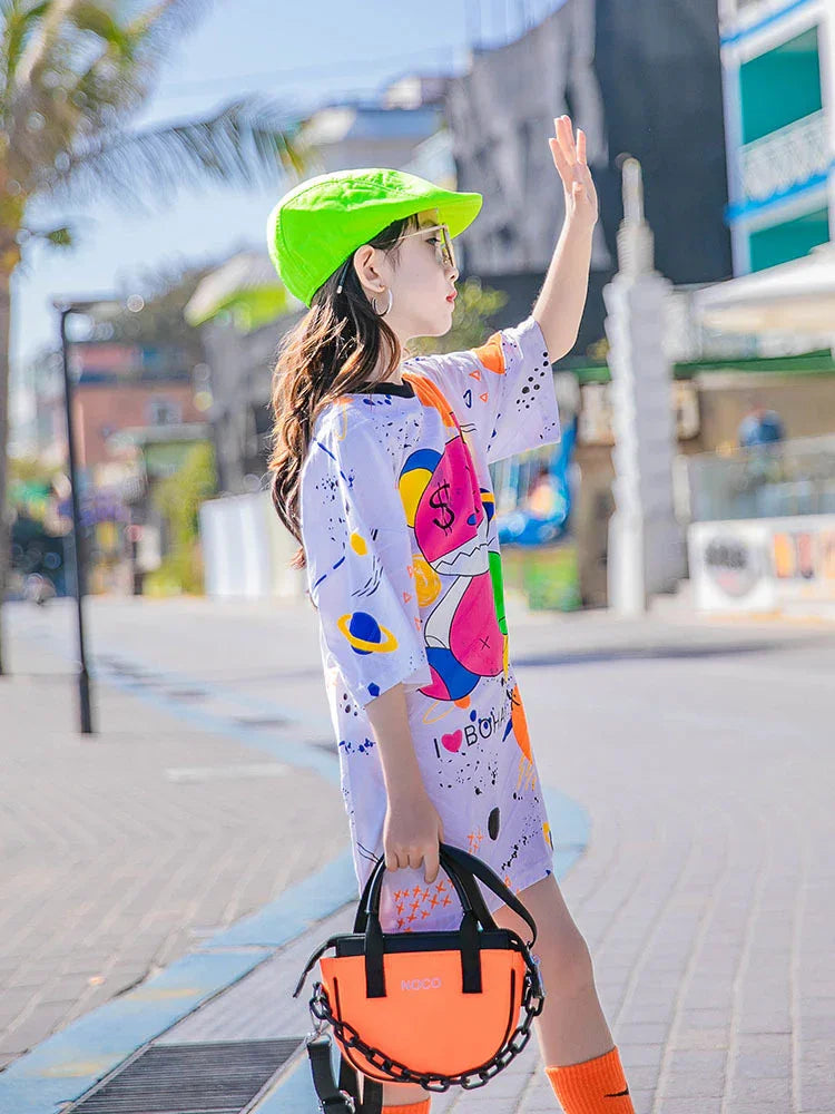 Woman in a loose colorful graphic t-shirt dress, neon green cap, and orange accessories