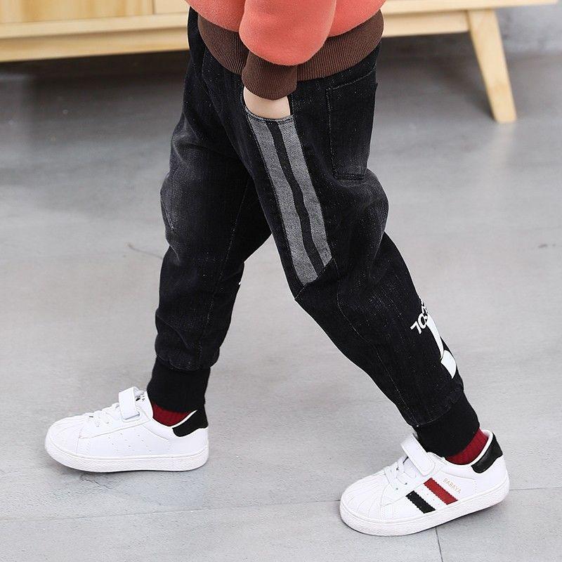 Child wearing black denim jogger pants with gray side stripes and white sneakers