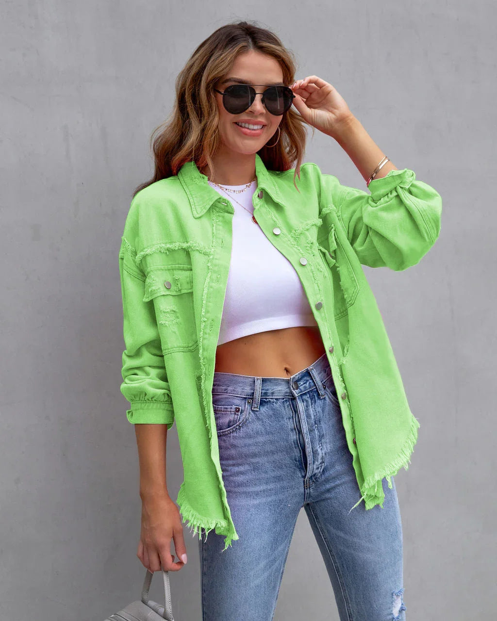 Woman wearing neon green oversized distressed denim jacket, white crop top, and blue jeans
