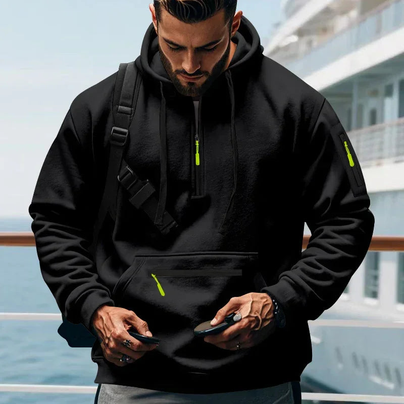 Man wearing black streetwear hoodie with neon green zippers, relaxed fit, drawstring hood, on a ship deck