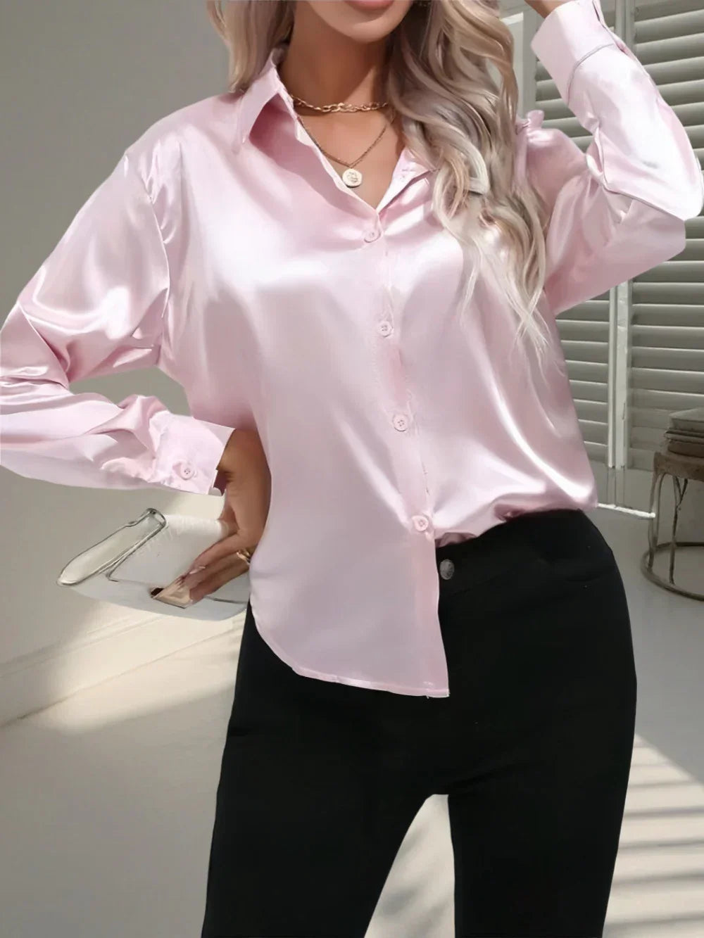 Woman wearing a loose-fit, long-sleeve light pink satin blouse with black pants