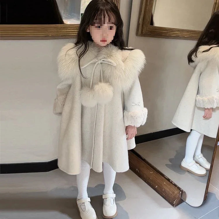 Girl wearing an ivory faux fur collar wool coat with pom-poms, white tights, and shoes