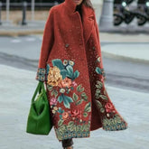 Woman wearing a long red wool coat with floral embroidery and relaxed fit, holding green bag