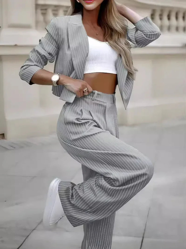Woman in grey pinstripe suit with cropped blazer, wide-leg pants, and white crop top
