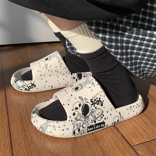 White platform slides with black space-themed cartoon print, worn with socks on wood floor