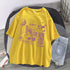 Yellow oversized short-sleeve graphic t-shirt with purple futuristic prints, paired with light wash denim shorts.