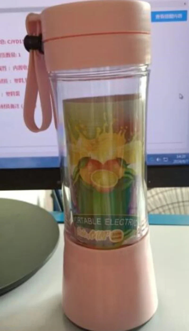 Pink portable electric blender cup with clear body and wrist strap on desk