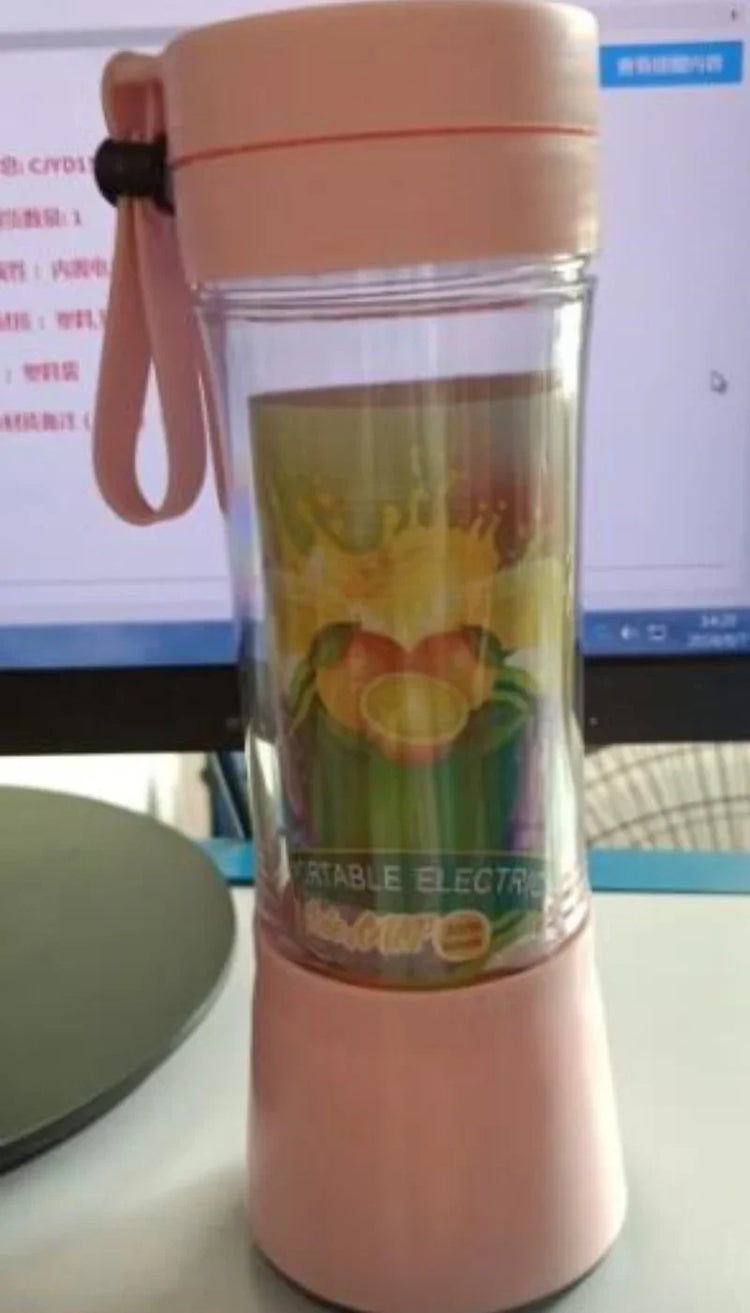 Pink portable electric blender cup with clear body and wrist strap on desk
