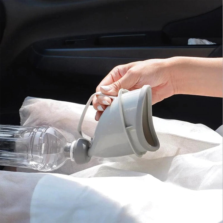 Hand holding a gray silicone portable urinal with ergonomic fit and clear plastic bottle in car