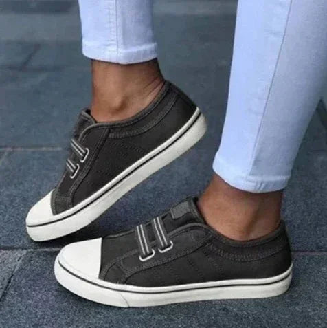 Black slip-on canvas sneakers with white soles and toe caps, worn with light jeans