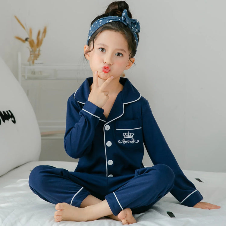 Girl in navy blue cotton pajama set with white piping, sitting cross-legged on bed