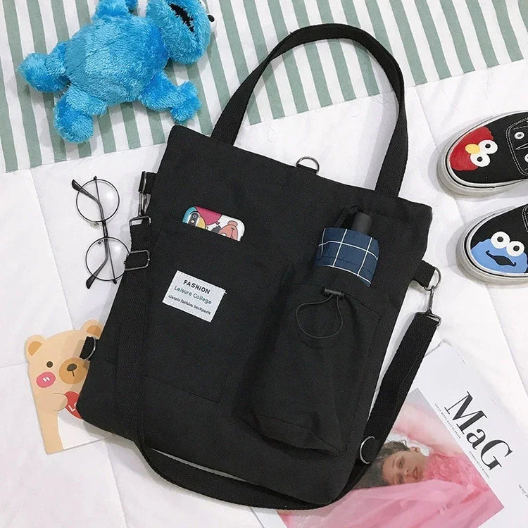 Black canvas tote bag with pockets, adjustable strap, casual streetwear style, relaxed fit