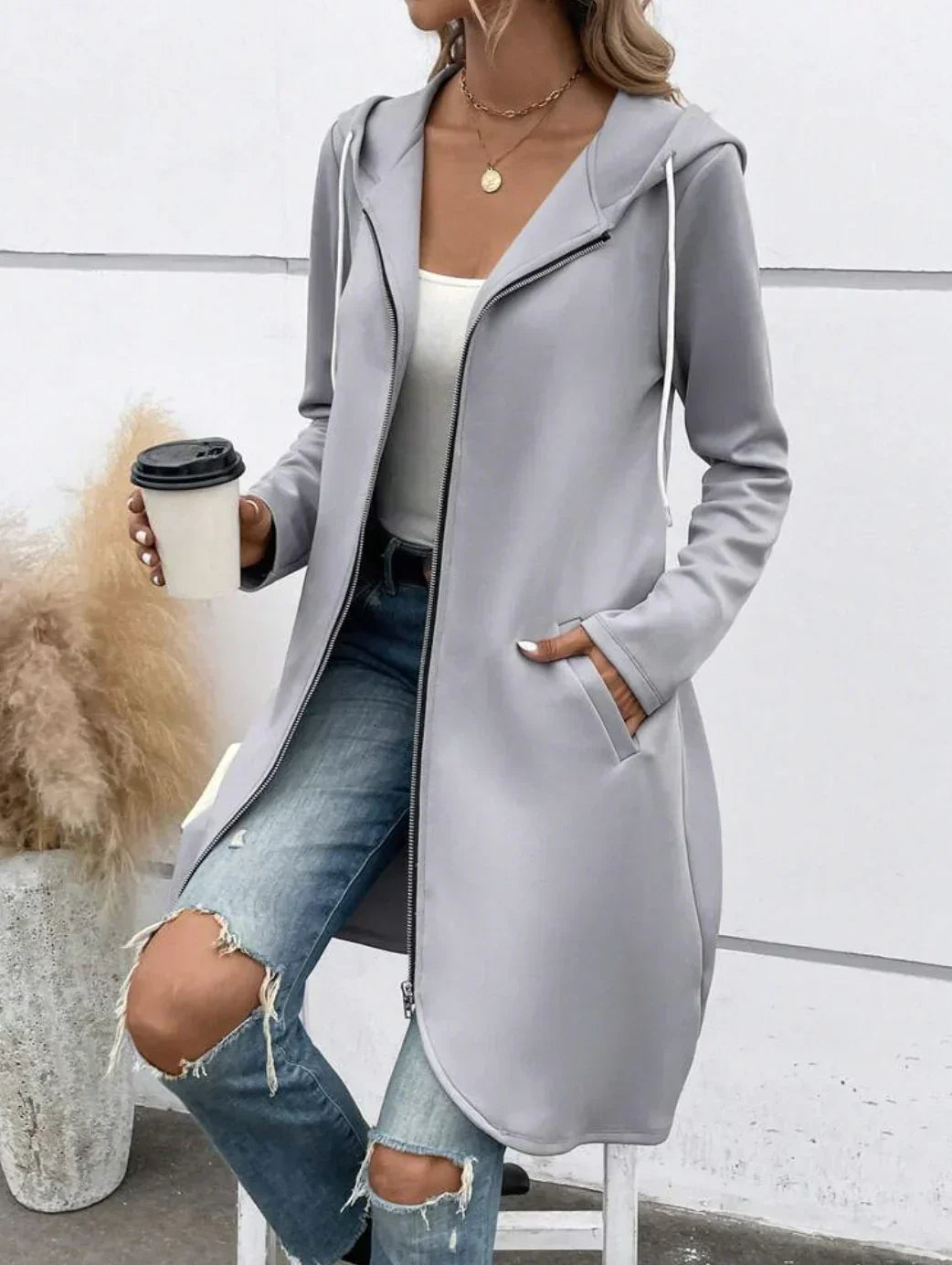 Woman wearing light gray long zip hoodie, white tank top, ripped blue jeans, casual streetwear