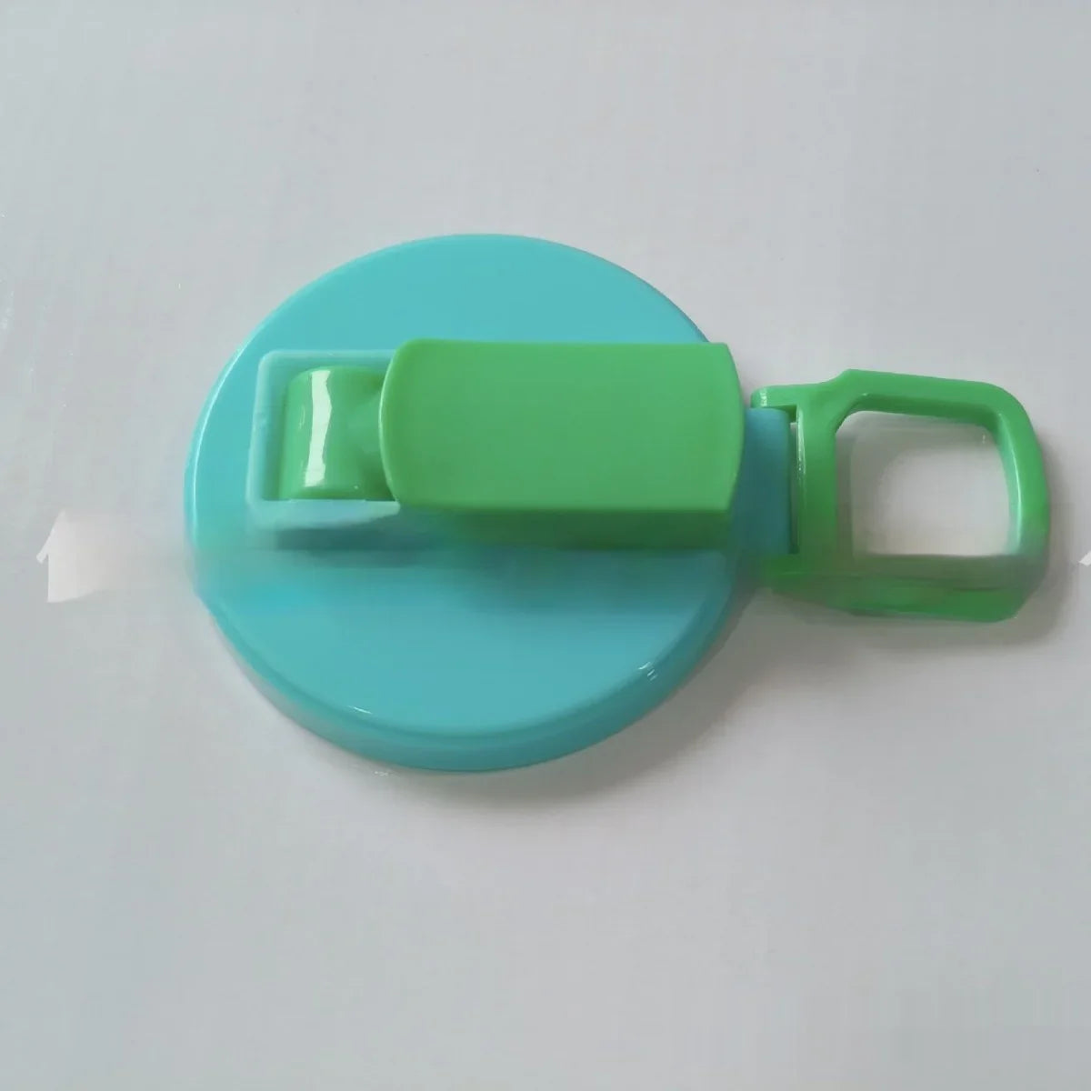 Blue and green plastic clip with round base and handle on a white surface