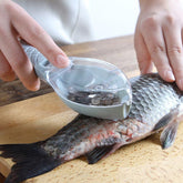 Hand using plastic fish scaler tool to remove fish scales on a cutting board