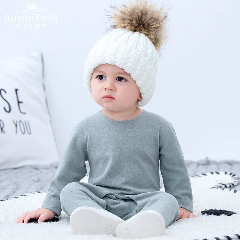 Baby in a light grey long sleeve cotton jumpsuit and chunky white knit beanie with faux fur pom pom, relaxed fit